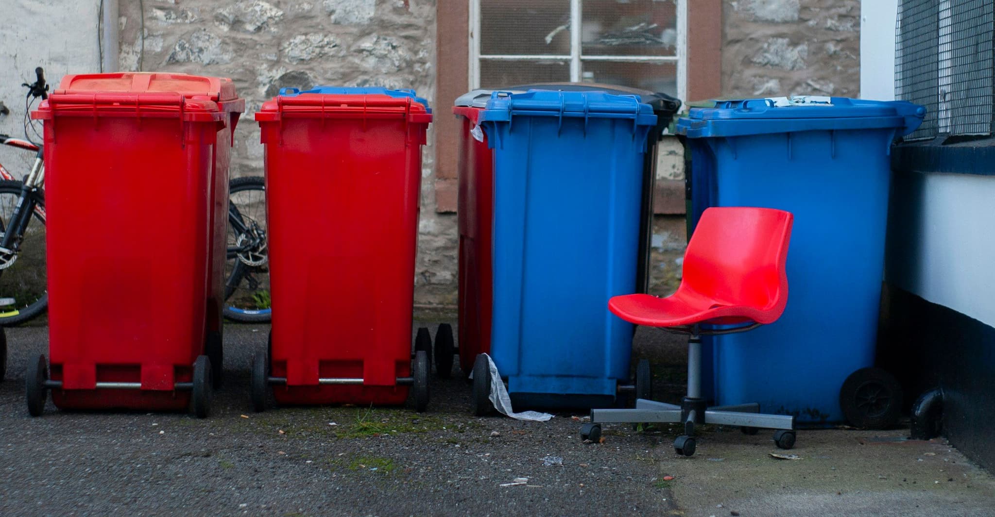 Four coloured wheelie bins next to a red chair